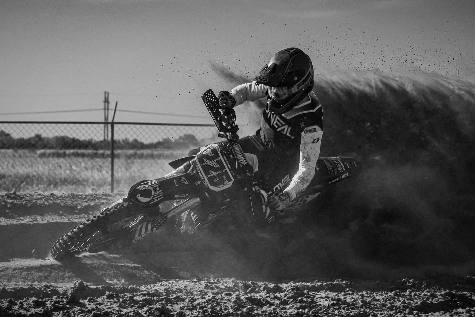Rider leaning the #225 bike through a sandy corner, throwing a wall of roost